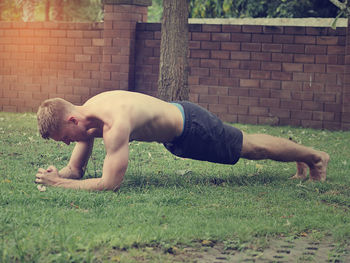 Side view of young man with arms raised on grass