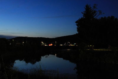 Silhouette trees by lake against sky at night