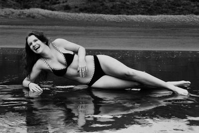 Happy teenage girl in bikini lying on shore at beach