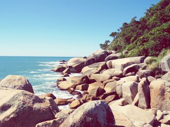 Rocks by sea against clear blue sky