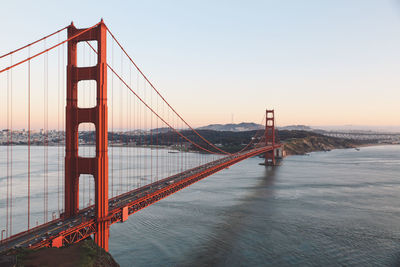 Suspension bridge over river against sky in sunset