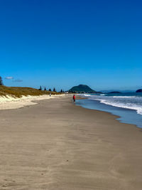 Person walking at beach against blue sky