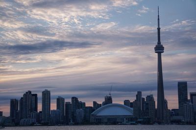 Lake ontario against cn tower amidst modern buildings at sunset