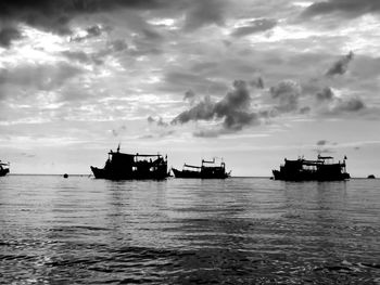 Boats in calm sea against cloudy sky