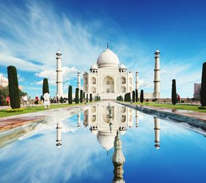 Taj mahal reflecting on pond against blue sky during sunny day