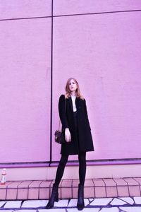 Full length portrait of woman standing against wall