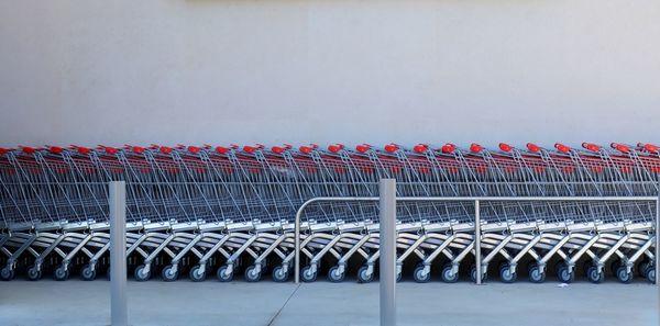 A row of empty metal carts near a supermarket near the background of a gray wall.