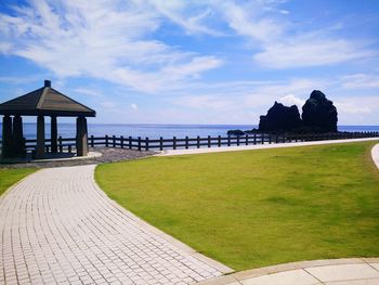 Footpath by sea against cloudy sky