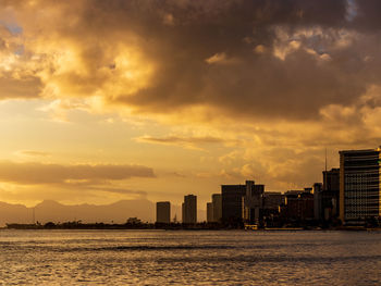 Sea by buildings against sky during sunset