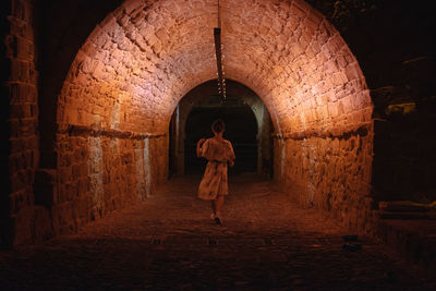 Rear view of woman walking in illuminated tunnel