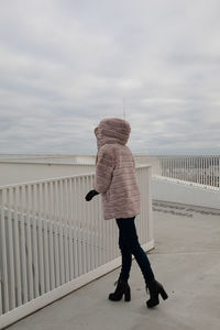 Rear view of woman standing on railing against sky