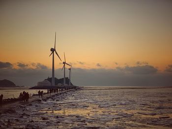 Scenic view including wind power generator of sea against sky during sunset
