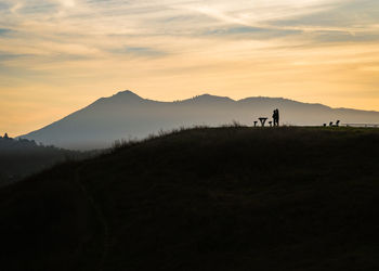 Silhouette couple standing on mountain against sky during sunset