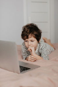 Little boy lie in the bedroom on the bed and look at the laptop. high quality photo