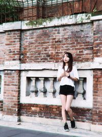 Full length portrait of young woman standing against brick wall