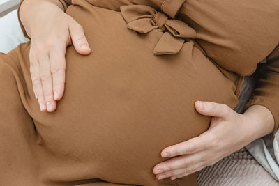 A pregnant woman is holding her belly with her hands, lying on the bed, top view, close-up.