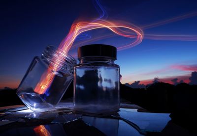 Close-up of illuminated glass jar on table against sky at night
