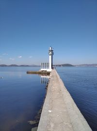 Lighthouse by sea against blue sky