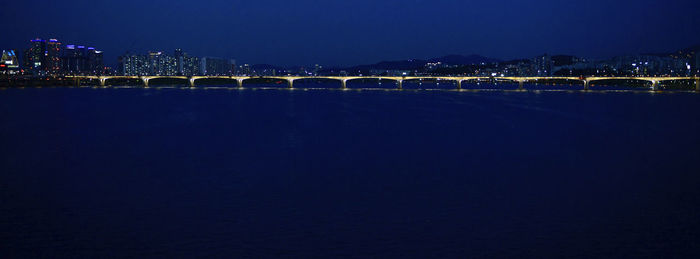 Illuminated city by sea against sky at night