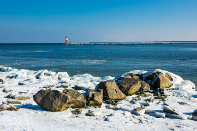 Frozen rocks at beach against clear sky