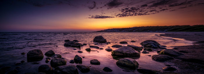 Rocks on beach against sky during sunset