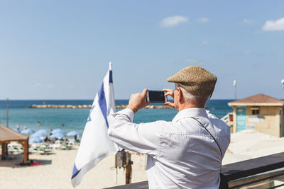 Rear view of man photographing sea against sky