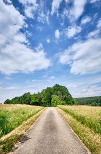 Empty road amidst field against sky