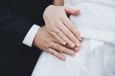 Midsection of bride and groom wearing wedding rings