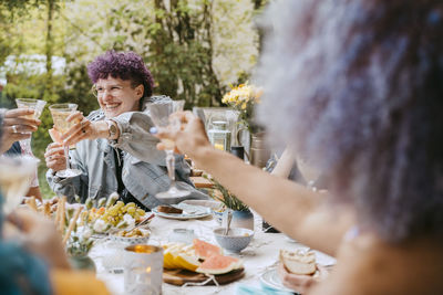 Cheerful non-binary person toasting drinks with friends during party in back yard