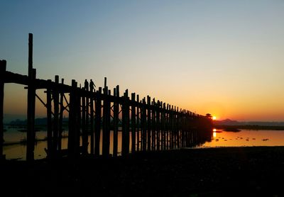 Silhouette pier on lake against clear sky during sunset