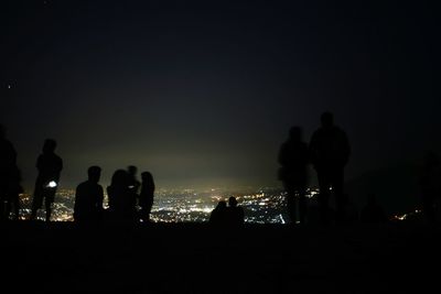 Silhouette people in illuminated city against sky at night