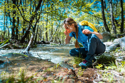 Woman refreshing herself with fresh water from clear creek while hiking