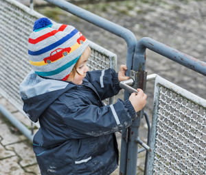 Side view of girl holding metal gate during winter