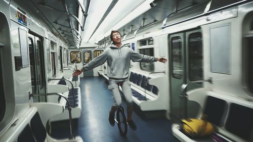 Full length of man with arms outstretched riding unicycle in train