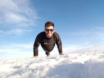 Portrait of man doing push-ups on snow against sky 