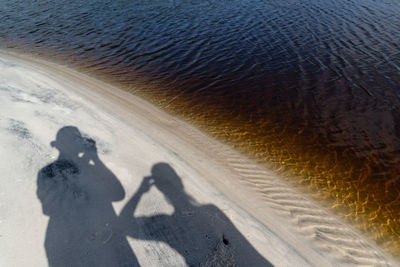 Shadows of a man and a woman on the beach sand by the water. 