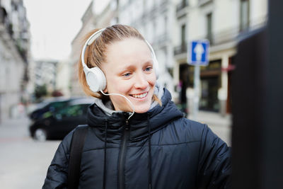 Smiling young woman listening to music using parking meter in city