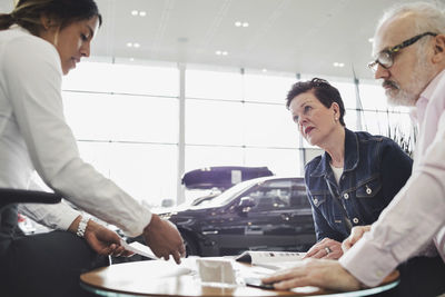 Saleswoman explaining documents to customers at car showroom