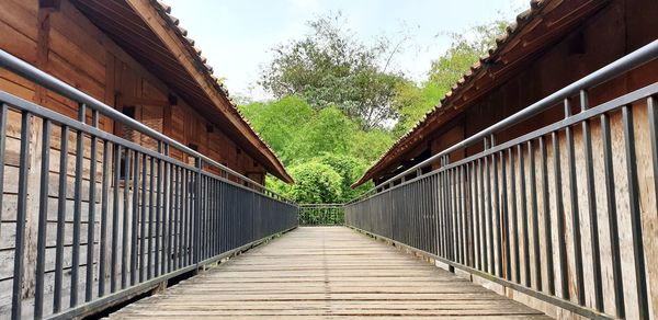 Empty footbridge amidst trees against sky