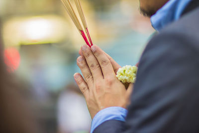 Cropped hands of man holding incense sticks with floral garland in temple