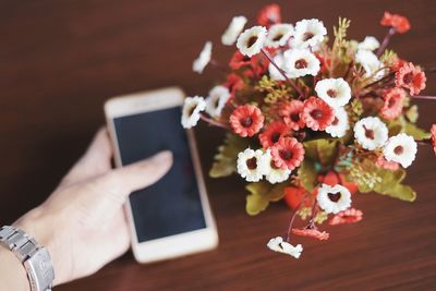 Cropped hand of person holding mobile phone by flowers on table