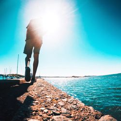 Rear view of man running on retaining wall by sea during sunny day