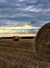 Hay bales on field against sky during sunset