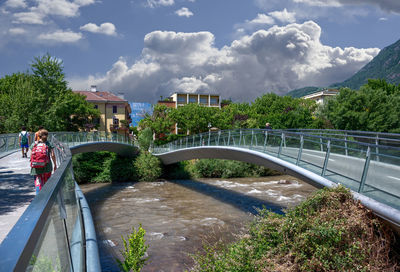 Woman on footbridge against plants and bridge against sky