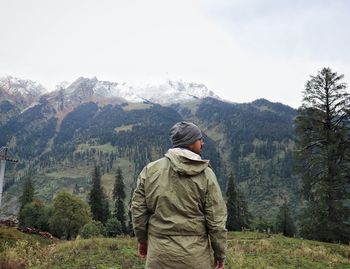 Rear view of man standing on grass against mountains and sky