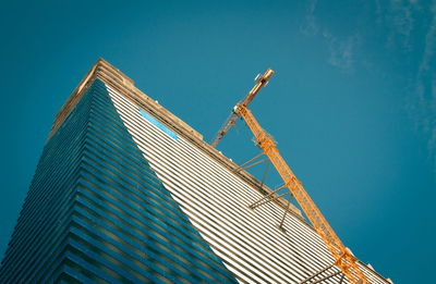 Low angle view of crane by building against clear blue sky