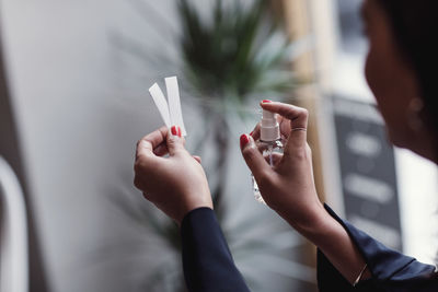 Cropped image of woman spraying perfume on litmus strips at workshop