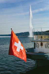 A swiss flag floating in the wind against the geneva lake and water fountain