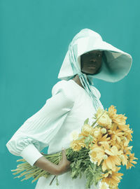 Portrait of woman wearing hat holding flowers against blue background