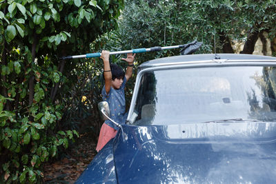 Side view of 8 years old girl with dark short hair brushing the roof of blue car